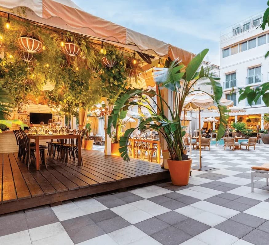 The poolside dining terrace at The Plymouth at dusk, under string lights and hanging greenery